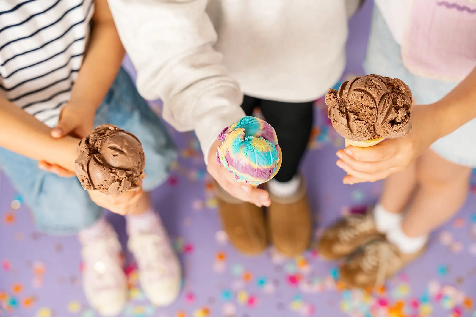 Three children holding ice cream cones with a colorful confetti background