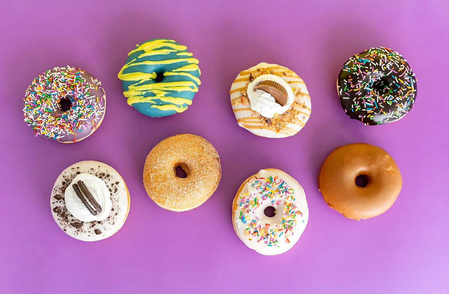 Assorted donuts with different glazes and sprinkles on a purple background