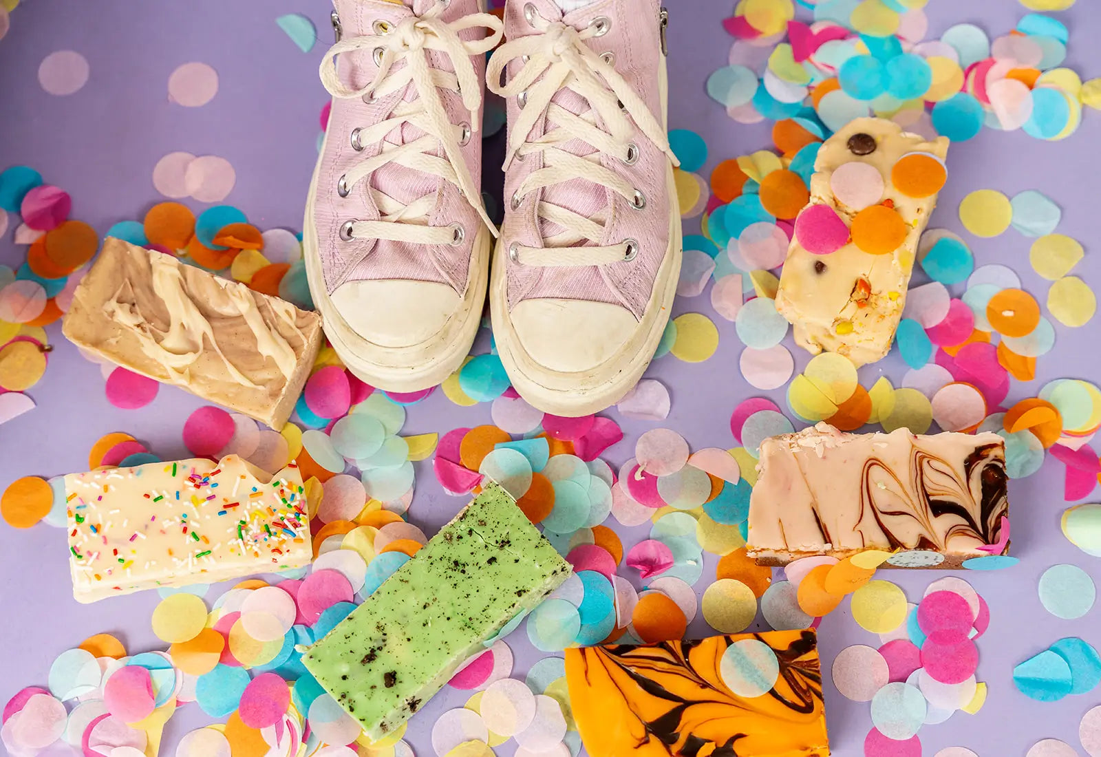Pair of pastel sneakers on a colorful confetti background with fudge bars.